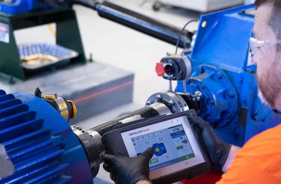 STR Mechanical technician using a ROTALIGN laser alignment system to align a motor-to-pump coupling, with the laser beam visible across the shafts.